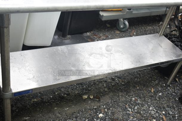 Commercial table with under shelf, stainless steel, visible wear, sturdy construction, ideal for kitchen use.