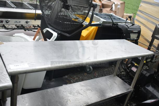 Commercial stainless steel table with under shelf, showing moderate wear. Includes visible markings and scuff marks.