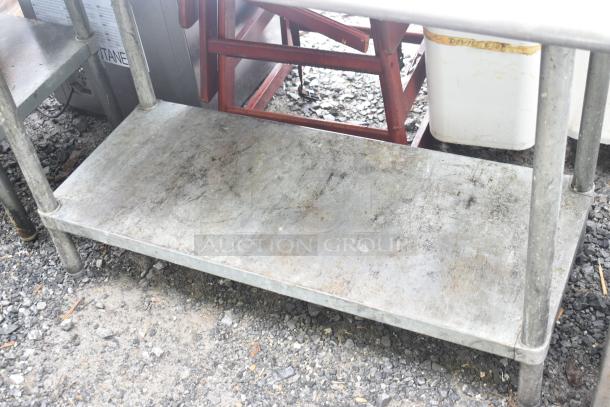 Commercial metal table with under shelf, showing surface wear. Sturdy design, ideal for kitchen or industrial use.