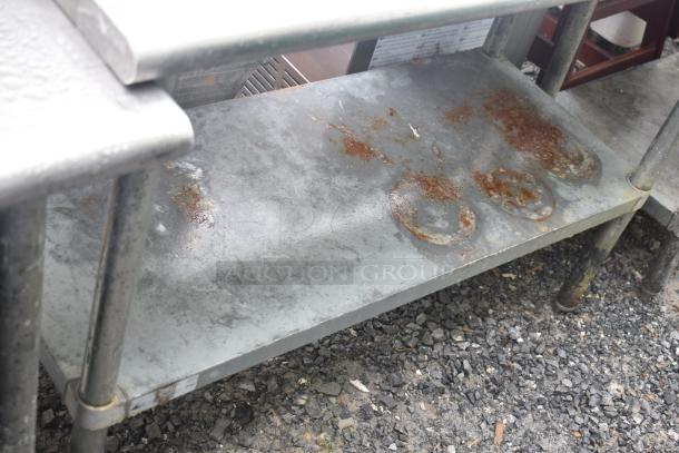 Commercial metal table with under shelf, visible rust and wear, sturdy legs, suitable for kitchen or workshop use.