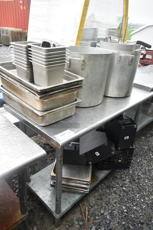 Commercial table with under shelf, holding aluminum stock pots, stacks of drop-in bins, and trays. Visible wear present.