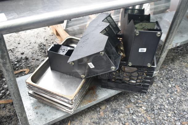 Commercial table with under shelf, containing black drop-in bins, metal stock pots, and trays. Rugged condition. Tags visible.