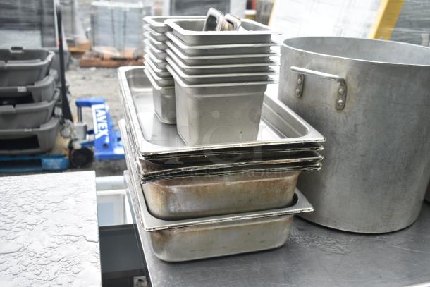 Commercial table with under shelf, containing stack of drop-in bins and large stock pot. Visible wear and stainless steel construction.