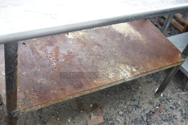Commercial table with under shelf, metal frame, showing visible rust and wear. Useful for industrial settings.