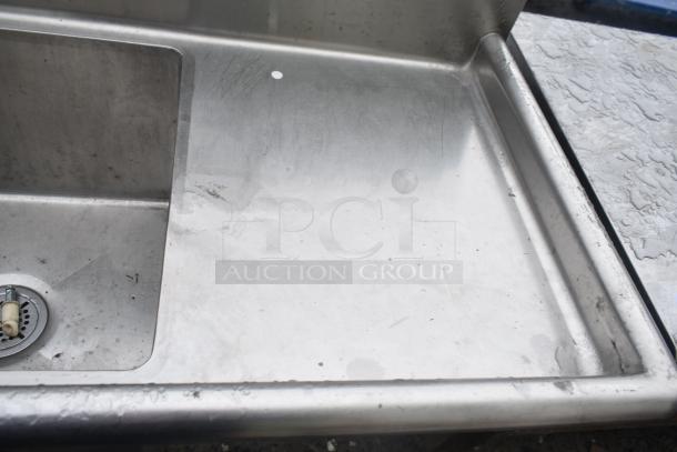 Commercial 3 bay sink with dual drain boards, stainless steel finish, moderate wear, sturdy construction.