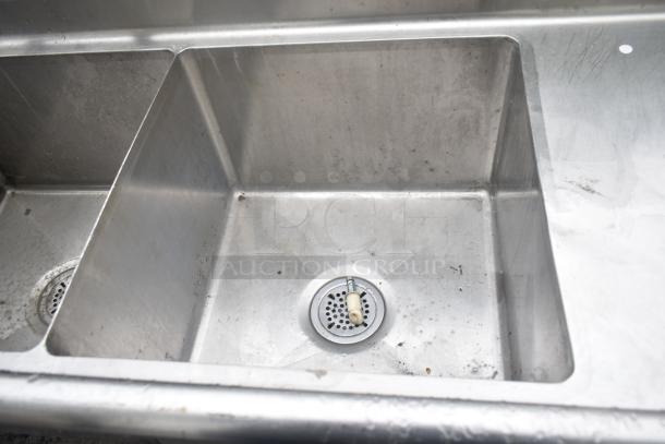 Commercial 3 bay sink with dual drain boards, stainless steel, visible wear and stains, includes drains and hardware.