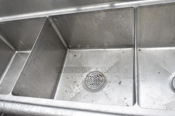Commercial 3 bay stainless steel sink with dual drain boards, visible wear, ideal for restaurant use.