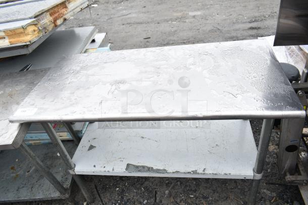 Commercial table with under shelf, stainless steel, weathered condition, visible wear and tarnish, sturdy metal legs.
