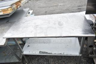 Commercial table with under shelf, stainless steel, weathered condition, visible wear and tarnish, sturdy metal legs.