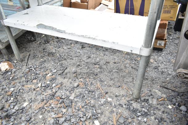 Commercial table with under shelf, metal frame, showing signs of wear and visible surface scratches.