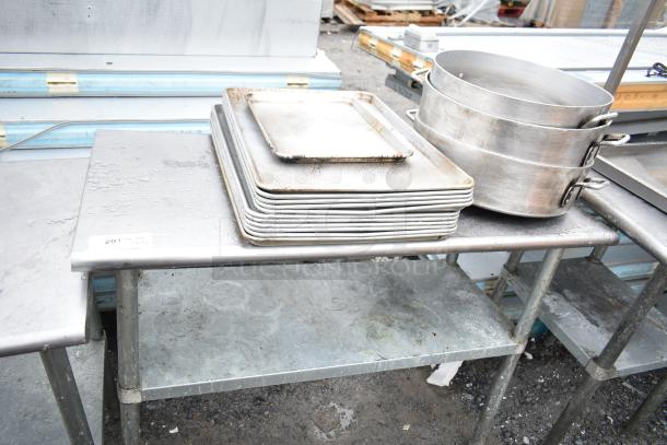 Commercial metal table with under shelf, includes stacked baking pans and round pots. Visible tag reads "201." Weathered condition.