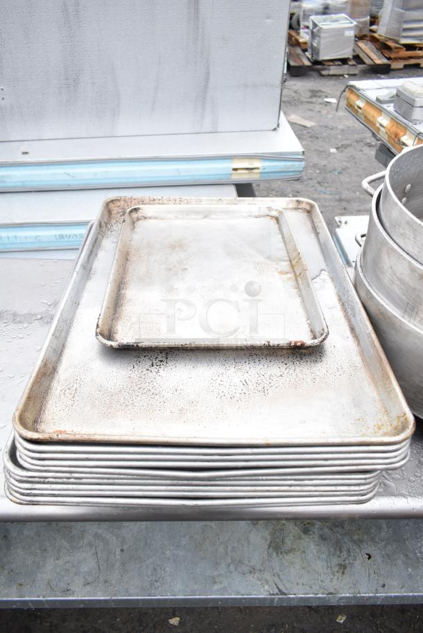 Stack of used baking pans on a commercial table with an under shelf, showing signs of wear.