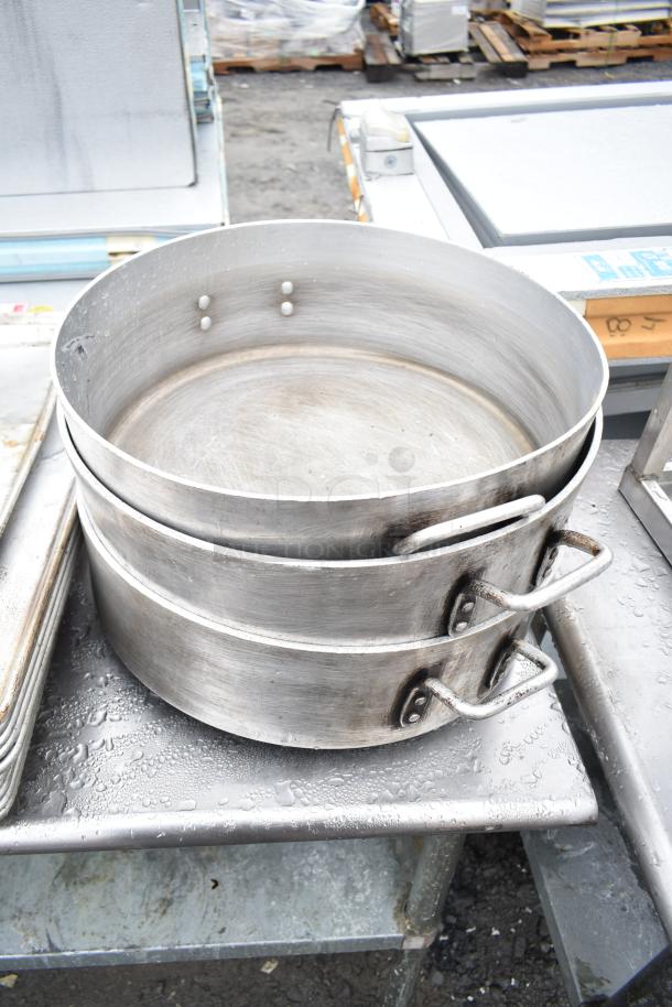 Commercial table with metal under shelf, featuring large stackable baking pans; visible wear and moisture on surfaces.