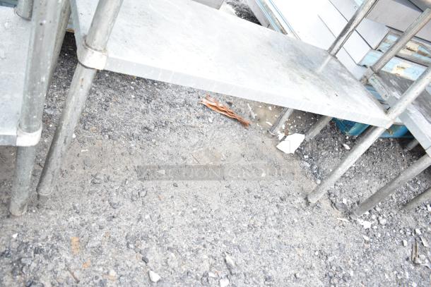 Commercial metal table with under shelf, holding baking pans. Slightly worn, suitable for kitchen or bakery use.