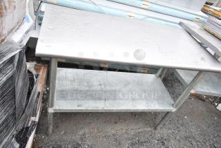Stainless steel commercial table with under shelf, used condition, visible surface wear, no visible markings.