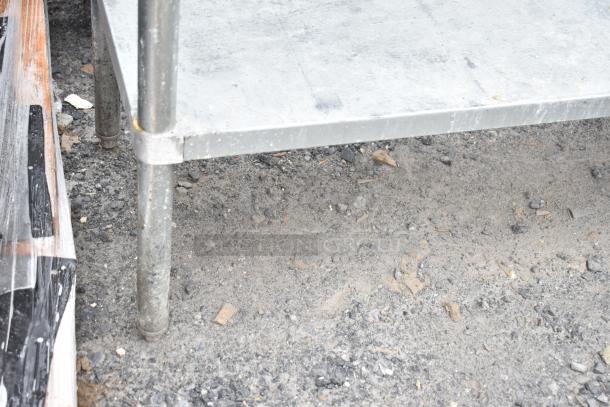 Commercial table with under shelf, metal construction, sturdy legs, some surface wear, ideal for industrial use.