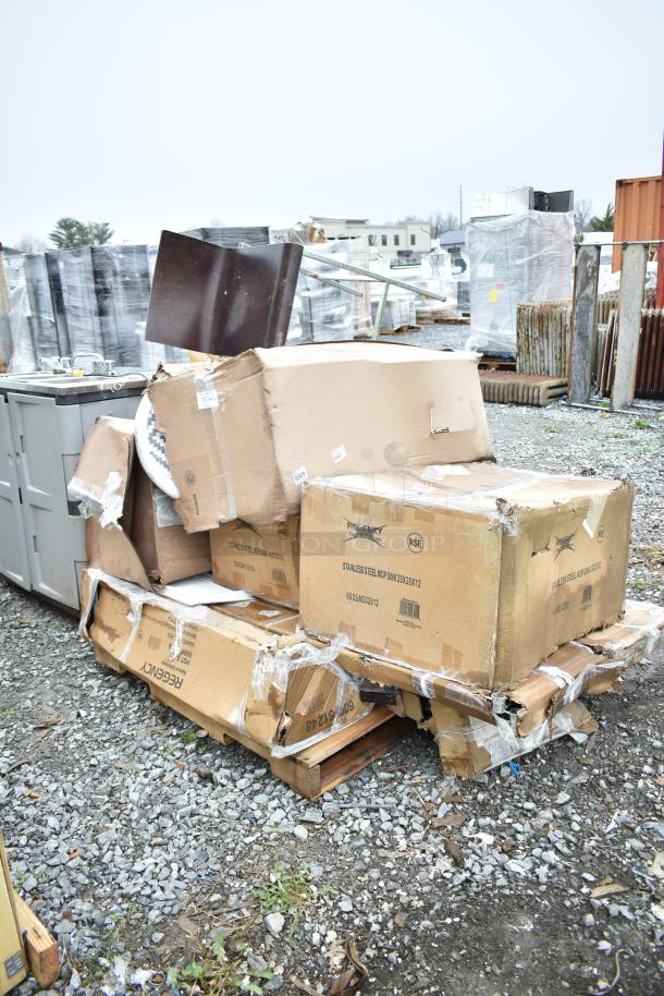 Damaged boxes labeled Regency, containing new scratch and dent items like a pot rack and mop sink, on gravel lot.