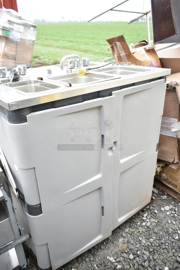 Portable sink with dual basins and chrome faucets, light gray body, visible wear, ideal for events or outdoor settings.