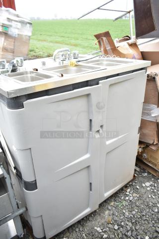 Portable sink with dual basins and chrome faucets, light gray body, visible wear, ideal for events or outdoor settings.