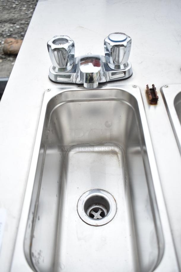 Stainless steel portable sink with chrome faucet and dual handles, showing slight wear.