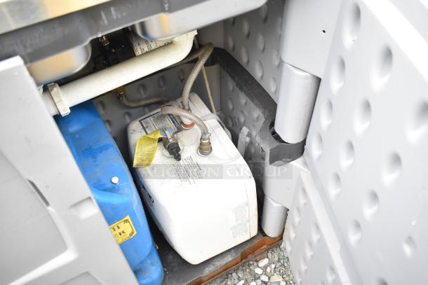 Underside view of a portable sink showing plumbing, blue water tank, and a white water heater with visible labels and fittings.