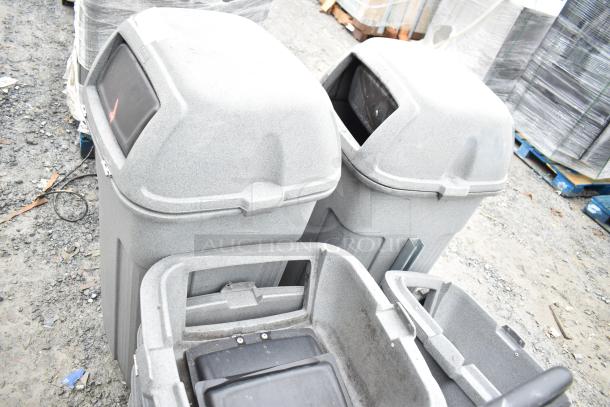 Two gray poly trash cans with seven lids, lightly used, showing design with hinged lids on gravel surface.