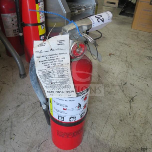 Koorsen ABC fire extinguisher in red, featuring visible service tags and instructions. Appears in used condition.