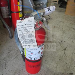 Koorsen ABC fire extinguisher in red, featuring visible service tags and instructions. Appears in used condition.