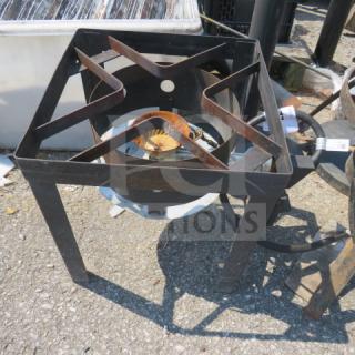 Heavy-duty metal gas burner with square frame, rusting visible, outdoor setting. Ideal for high-heat cooking.