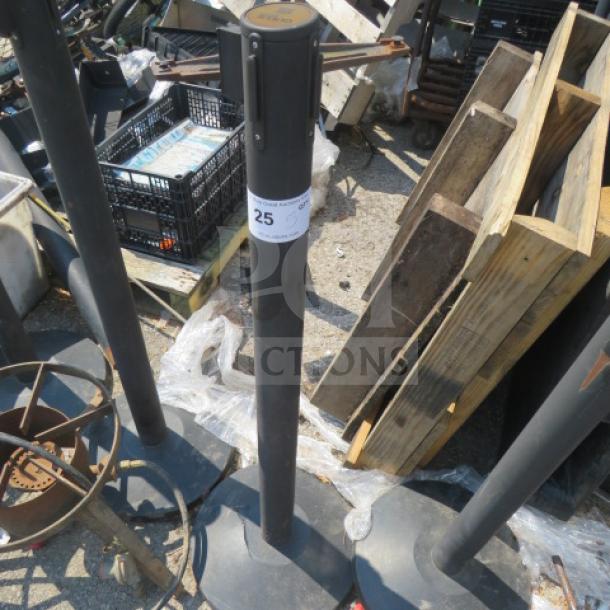 Crowd control pole, black, model 5XBID, sturdy base, visible label with number 25, signs of outdoor use.