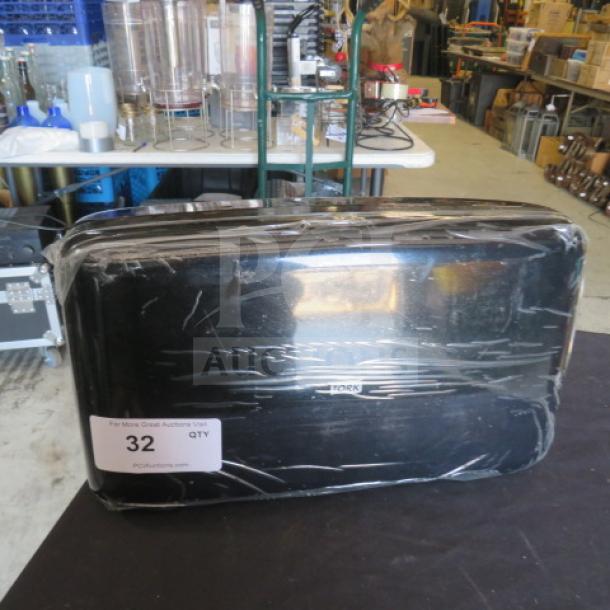 Black Tork toilet paper dispenser, wrapped in plastic, showing a label with auction lot number 32.