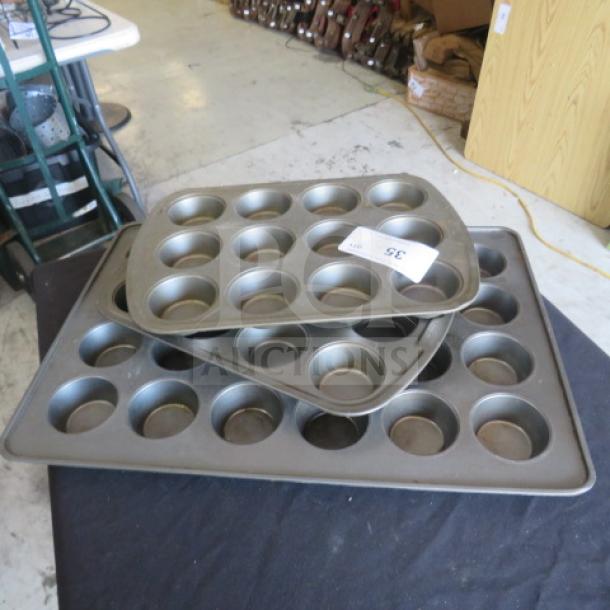 Assorted muffin tin set, three pieces, metal, standard size, used condition, auction label "35" visible.