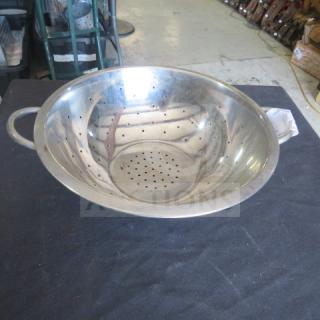 Stainless steel colander with dual handles, perforated for draining, in good condition on a dark surface.