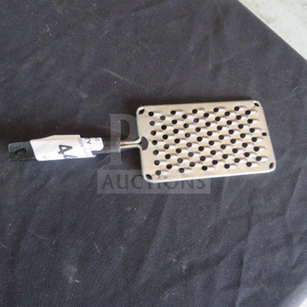 Metal hand grater with a black handle. Features large holes for grating, visible auction tag with number 44.