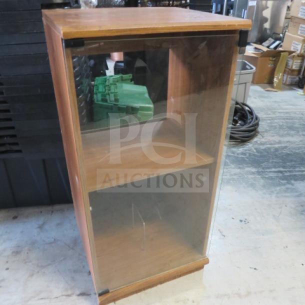 Wooden media case with glass door, measuring 18x16x38 inches. Features two shelves. Visible wear on the surface.