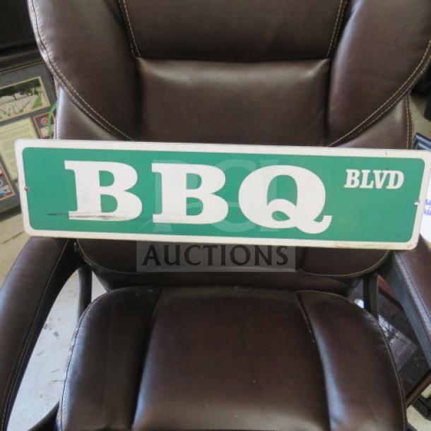 24x6 inch "BBQ BLVD" street sign with green background and white lettering, minor wear, displayed on a brown chair.