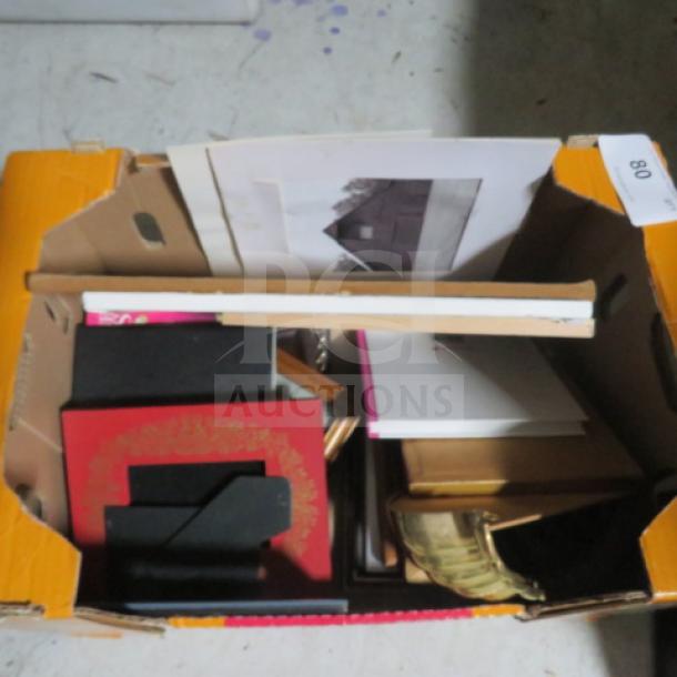 A cardboard box containing assorted items, including books, folders, and papers. Some items have ornate designs and gold edges.