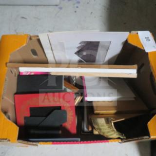 A cardboard box containing assorted items, including books, folders, and papers. Some items have ornate designs and gold edges.