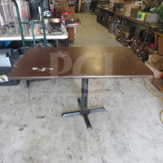 Brown laminate table top with pedestal base, measuring 48x30x28 inches. Visible wear and scratches on the surface.