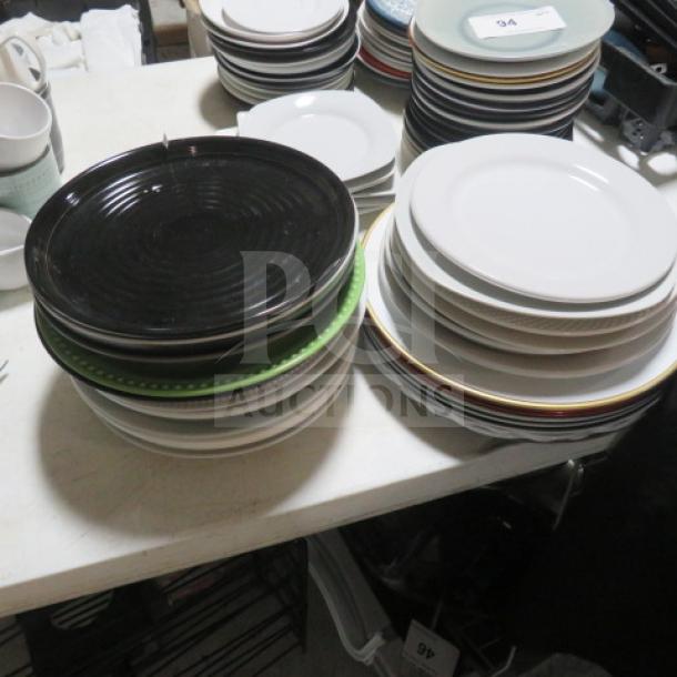 Assorted plates mega lot on table, various colors and sizes, good condition, includes black, white, and green plates.