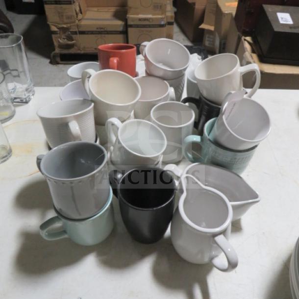 Assorted coffee cups in various colors and styles, stacked on a table, showing mix of modern and classic designs.