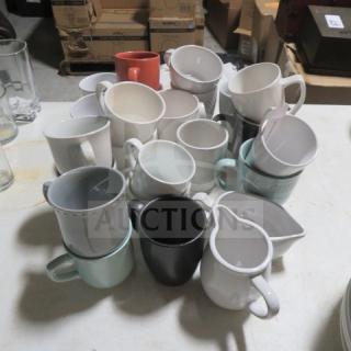 Assorted coffee cups in various colors and styles, stacked on a table, showing mix of modern and classic designs.