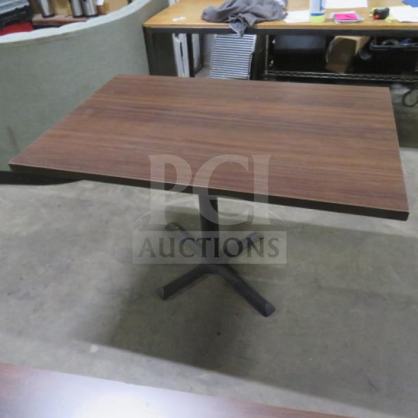 Brown laminate table top on a black pedestal base, measuring 45x30x30 inches. Good condition, ideal for office or dining use.