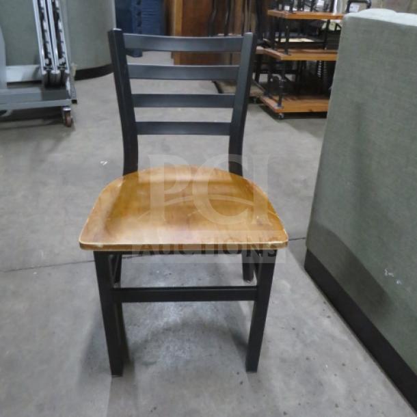 Black metal chair with a wooden seat, featuring a ladder-back design. Shows signs of wear, suitable for various decor styles.