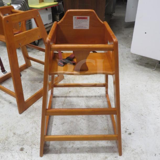 Wooden high chair with safety straps, natural finish. Includes backrest label for usage instructions. Sturdy condition.