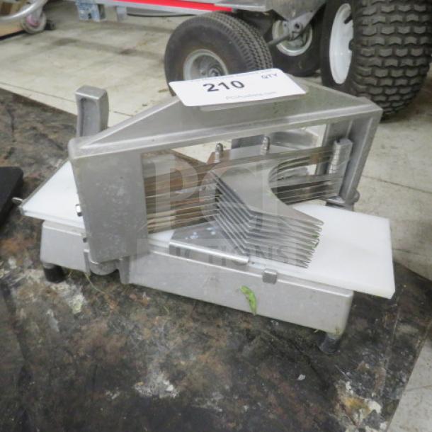 Heavy-duty metal tomato slicer with multiple sharp blades and a white cutting surface. Auction tag marked "210" attached. 