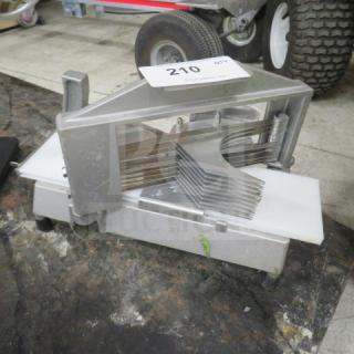 Heavy-duty metal tomato slicer with multiple sharp blades and a white cutting surface. Auction tag marked "210" attached. 