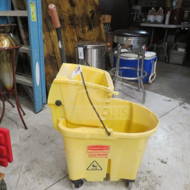 Rubbermaid yellow mop bucket with wringer, visible caution symbol, on casters, used condition.