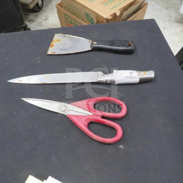 Assorted utensils: a putty knife with a black handle, a kitchen knife with a patterned handle, and red-handled scissors. Visible wear on knife blade.