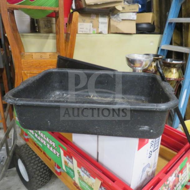 Black plastic bussing tub on a red wagon, showing signs of wear. Suitable for restaurant or catering use.